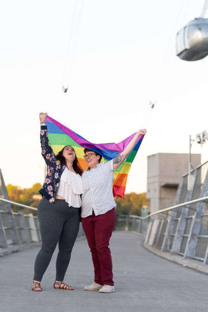 istock Female couple share a kiss underneath a Pride Flag while they stand on a bridge 1151067301