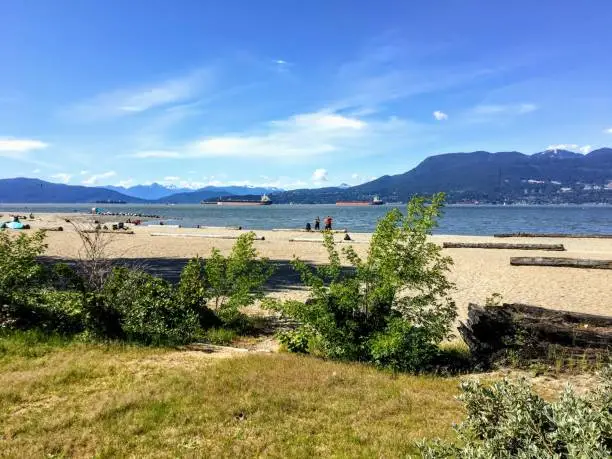 Photo of A beautiful view of the sandy beaches of Spanish Banks, with tankers and mountains in the background on a beautiful sunny day.  This is popular spot during the summer in Vancouver, Canada