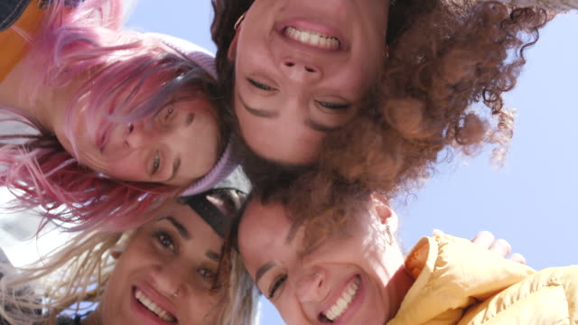 4 young smiling women in a group - heads together shot from below