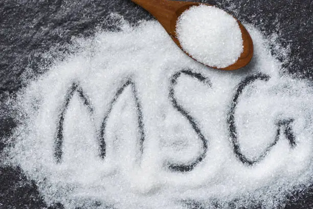 Photo of Heap of monosodium glutamate on wooden spoon and dark background - text MSG