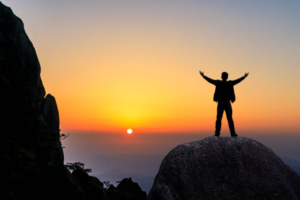 istock Hiker is standing on a rock with raised hands and enjoying sunrise 1151101946