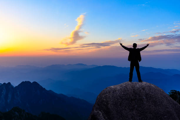 istock Hiker is standing on a rock with raised hands and enjoying sunrise 1151101990
