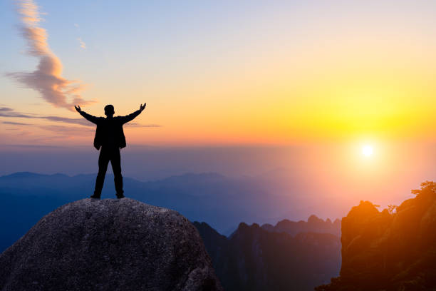 istock Hiker is standing on a rock with raised hands and enjoying sunrise 1151102009