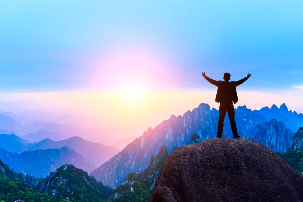 istock Hiker is standing on a rock with raised hands and enjoying sunrise 1151102050