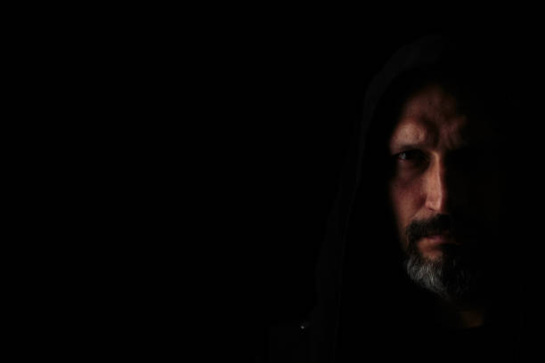 istock Brutal man with a gray beard in the hood with sharp shadows on a black background. Copy space. 1151105848