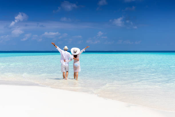 Couple walks down a tropical beach in white clothing