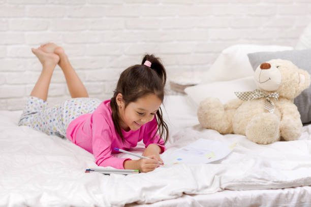 istock cute little girl drawing pictures while lying on bed 1151114828