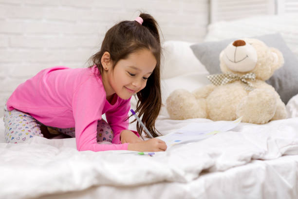 istock cute little girl drawing pictures while lying on bed 1151114845