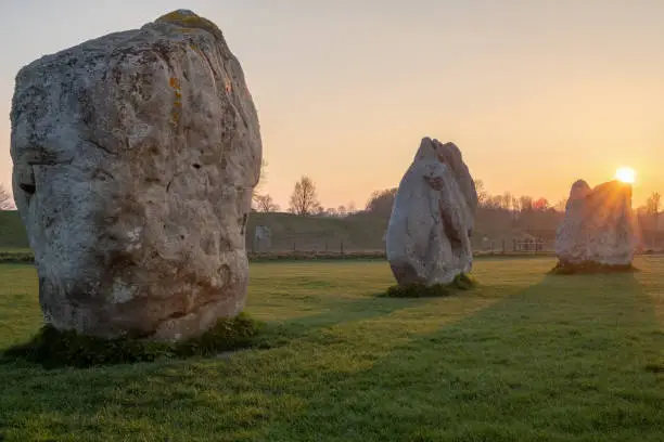 Prehistoric standing rocks at a golden sunset and the sun dipping behind the rocks in a field in Wiltshire, United Kingdom, nobody in the image