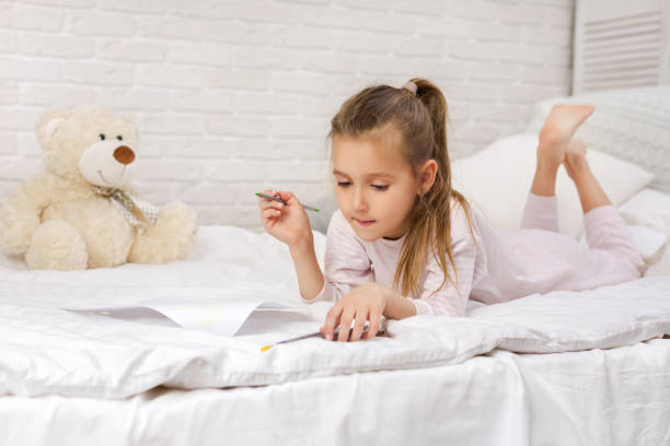 istock cute little girl drawing pictures while lying on bed 1151137828