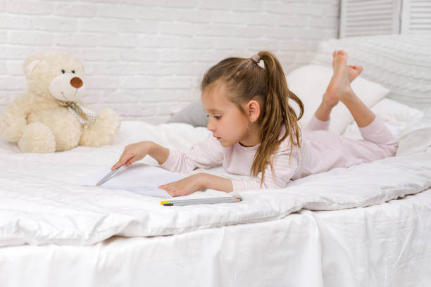 istock cute little girl drawing pictures while lying on bed 1151137846