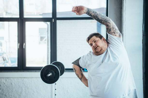 istock overweight tattooed man Looking At Camera and doing stretching exercise at gym 1151139746