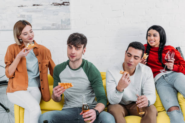 istock happy multicultural friends eating pizza and enjoying drinks while sitting together on yellow sofa 1151139997