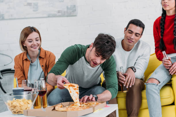 istock young man taking piece of pizza while multicultural friends enjoying drinks 1151140011