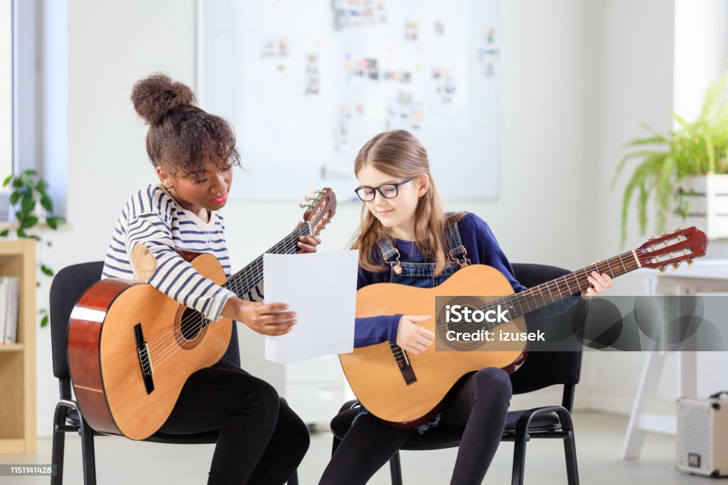 Music trainer showing sheet to female student Trainer showing sheet to student while practicing guitar. Pre-adolescent guitarist is learning with teacher in in training class. They are at education building. Child Stock Photo