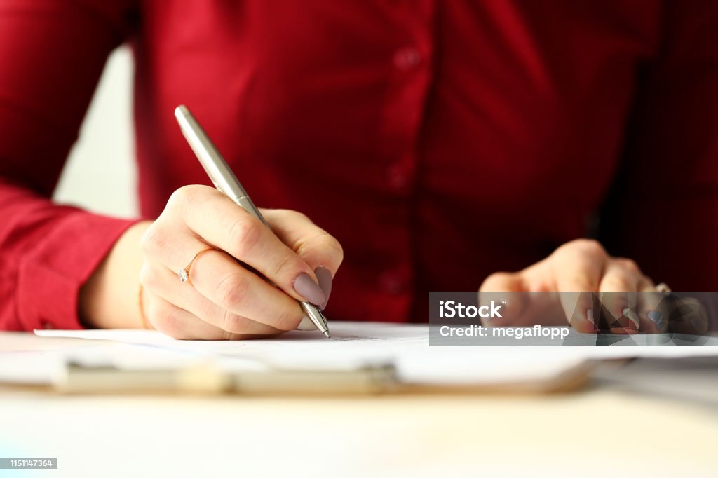 Female office worker holding silver pen filling out some application form Female office worker holding silver pen filling out some application form closeup Petition Stock Photo