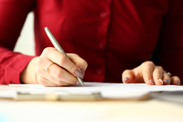 Female office worker holding silver pen filling out some application form Female office worker holding silver pen filling out some application form closeup petition stock pictures, royalty-free photos & images