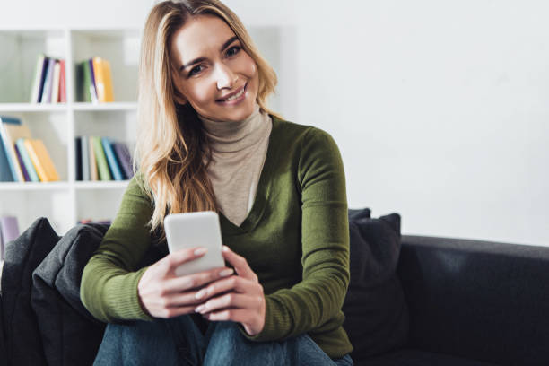 istock cheerful woman holding smartphone while sitting on sofa 1151148941