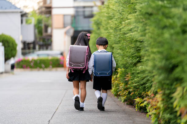 手をつないで一緒に学校に歩いている若い弟と妹 - ランドセル ストックフォトと画像