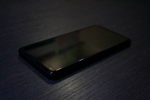 Modern glossy black smartphone isolated on dark wooden background