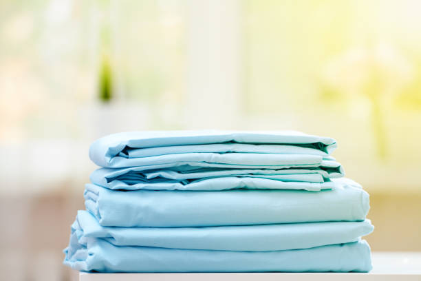 plan rapproché de la literie propre bleue sur un fond flou. une pile de nouvelles feuilles de lit pliées sur la table. lumière du soleil de la fenêtre. - drap photos et images de collection