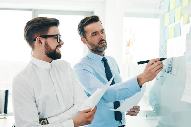 istock Two businessmen working together in modern office discussing new project on whiteboard 1151152152