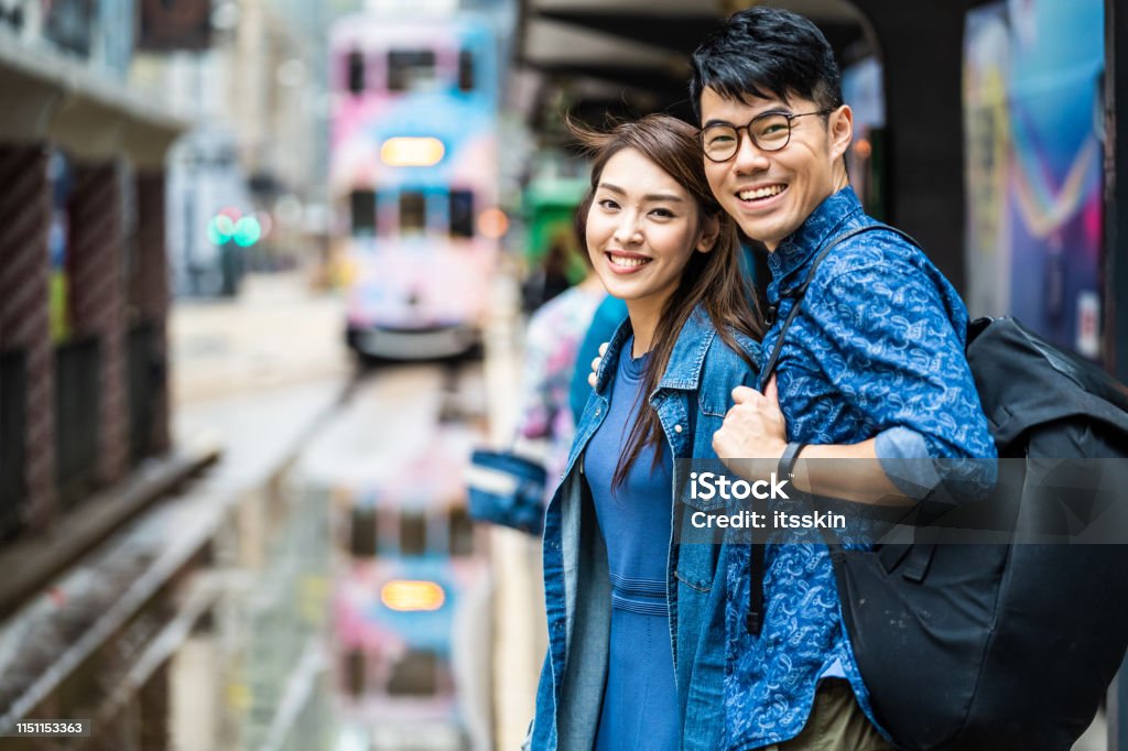 Two people are waiting for the tram in Hong Kong. Two people are waiting for the tram in Hong Kong. In the background the tram is arriving, reflection of the traffic on the wet ground. Chinese Culture Stock Photo