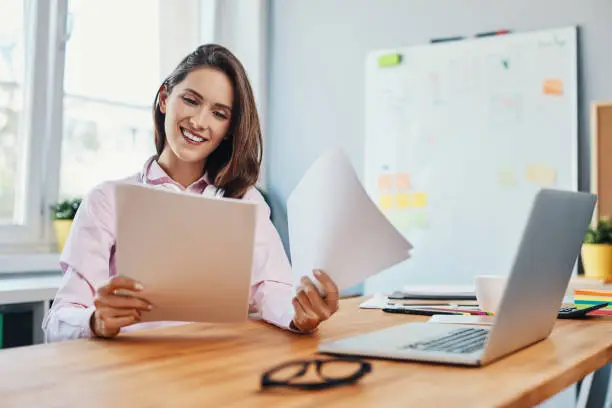 Smiling young woman looking at business documents working in home office