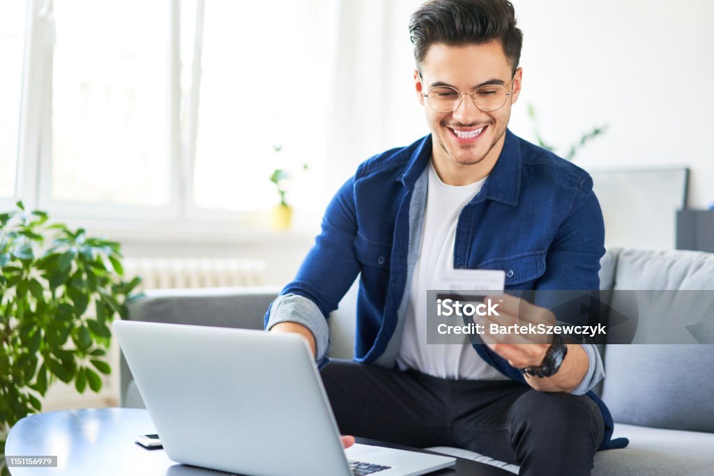 Cheerful young man using credit card and laptop to pay for shopping online Credit Card Stock Photo