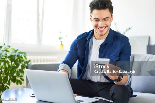 Cheerful Young Man Using Credit Card And Laptop To Pay For Shopping Online Stock Photo - Download Image Now