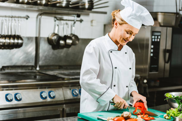 istock beautiful female chef in uniform cutting pepper in restaurant kitchen 1151159201