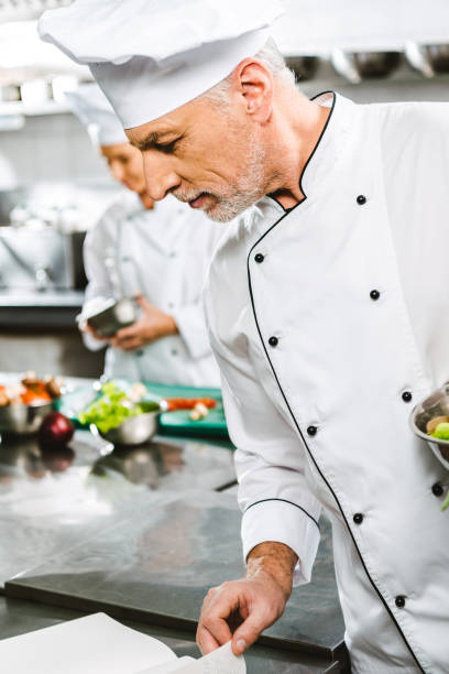 istock male chef in uniform and hat reading recipe book in restaurant kitchen 1151159255