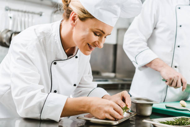 istock beautiful smiling female chef in uniform decorating dish with herb in restaurant kitchen 1151159270