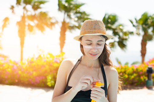 beautiful woman smears face sunscreen at the beach for sun protection.