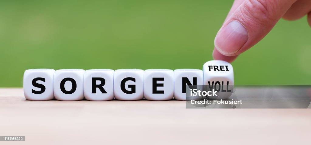 Hand turns a dice and changes the German word "sorgenvoll" ("sorrowful" in English) to "sorgenfrei" ("carefree" in English). Abstract Stock Photo