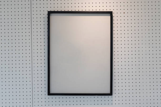 istock hanging empty black wooden picture frame on orderly dot or hole wall with orange light form ceiling. 1151178849