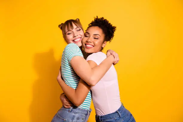 Portrait of charming cute pretty ladies cuddle tender gentle positive bun close eyes wear modern trendy style stylish t-shirt jeans wavy curly hairdo isolated on yellow background.