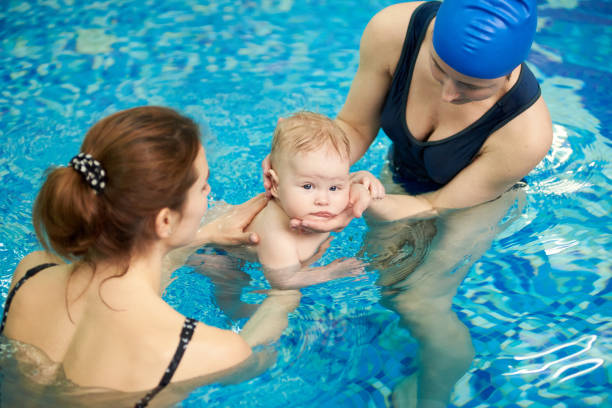 istock Swimmer baby looking in camera while immersing in water at swimming classes in paddling pool. Teaching swimming, diving 1151180681