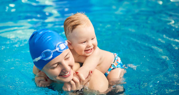 child having fun in water with mom. small wet boy smiling holging on his mother's back in pool. horizontal portrait view - mother enjoyment built structure human head imagens e fotografias de stock