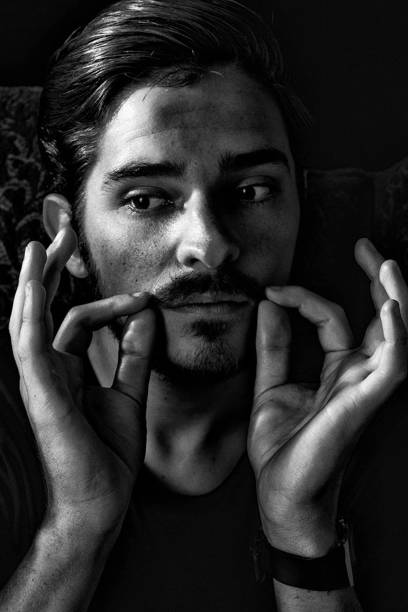 Close up of young adult male with moustache looking away expression finished in monotone, black and white. Concept for artist or acting school. Close up of young adult male with moustache looking away, expression finished in monotone, black and white. Concept for artist or acting school. man acting gangster stock pictures, royalty-free photos & images