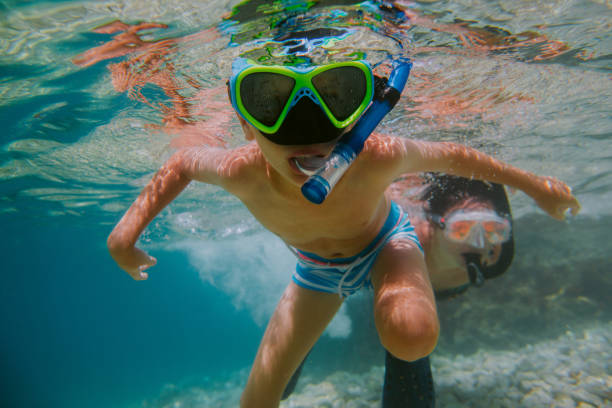 Child learning to snorkel with his mother in sea. Young boy wearing diving mask swimming under water. shallow stock pictures, royalty-free photos & images