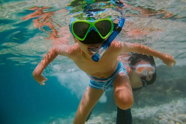 Photo of Child learning to snorkel with his mother in sea.
