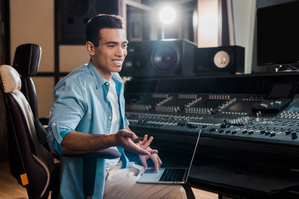 istock smiling mixed race sound producer sitting by mixing console and using laptop 1151191246