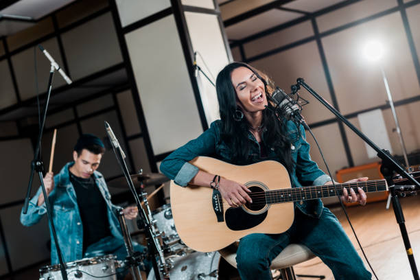 istock selective focus of beautiful inspired musician playing guitar and singing while mixed race man playing drums in recording studio 1151191451