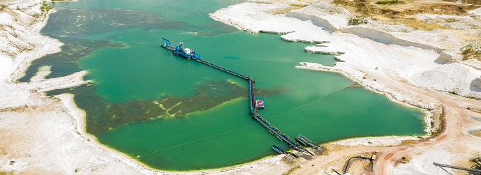 Aerial view of a blue-green quarry pond for quartz sand in Germany with the suction dredger and the conveyor belt for the sand