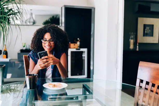 Young afro descendant teenager using smartphone during breakfast
