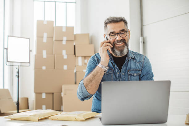 Always keep contact with customer Bearded men working on packaging and online delivery in home office business. He talking on phone with customer warehouse office stock pictures, royalty-free photos & images