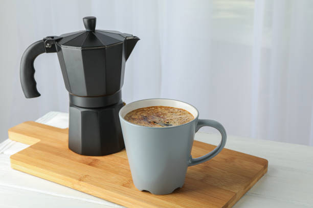 istock Cutting board with cup of fresh coffee and coffee maker on white table against light background, space for text 1151200170