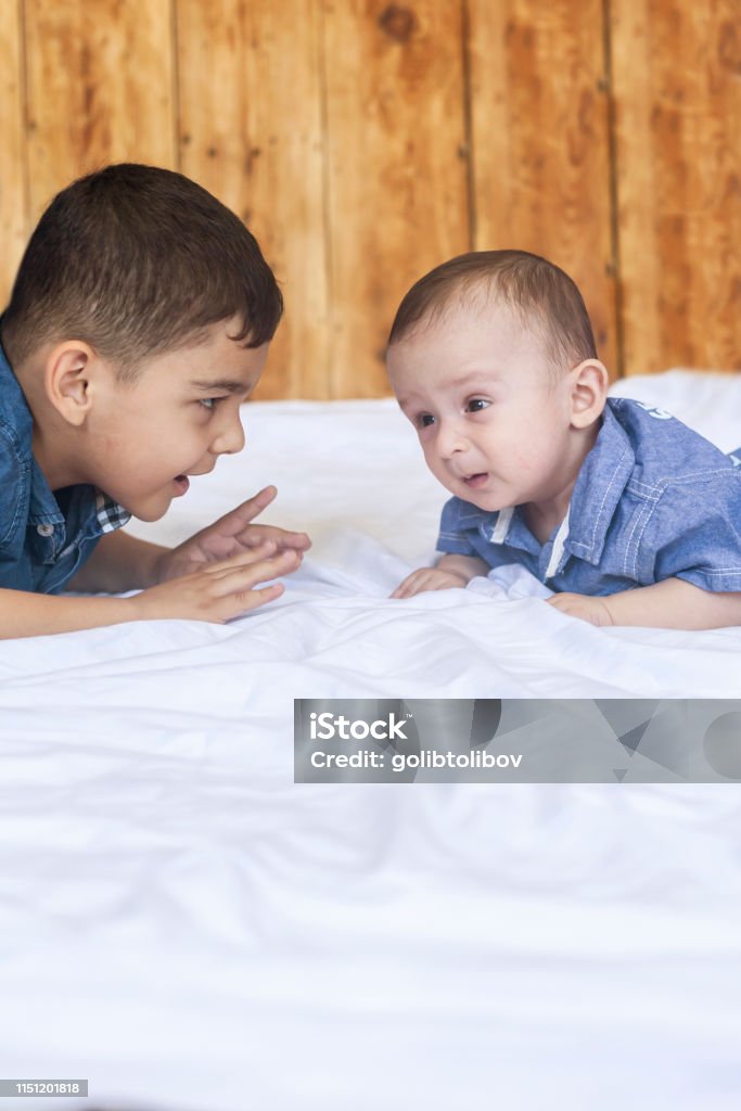 Happy brothers. Two cute little brothers lying on bed together Happy childhood concept. Happy brothers portrait. 6 years boy and 6 months old baby boy having fun. Two little kids smiling to the camera. View from above. Cute little brothers lying on bed together. 6-11 Months Stock Photo