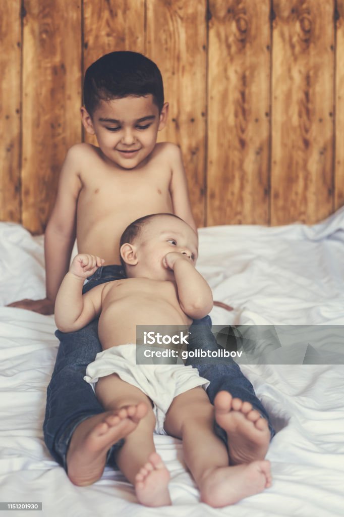 Happy brothers. Two cute little brothers lying on bed together Happy childhood concept. Happy brothers portrait. 6 years boy and 6 months old baby boy having fun. Two little kids smiling to the camera. View from above. Cute little brothers lying on bed together. 6-11 Months Stock Photo